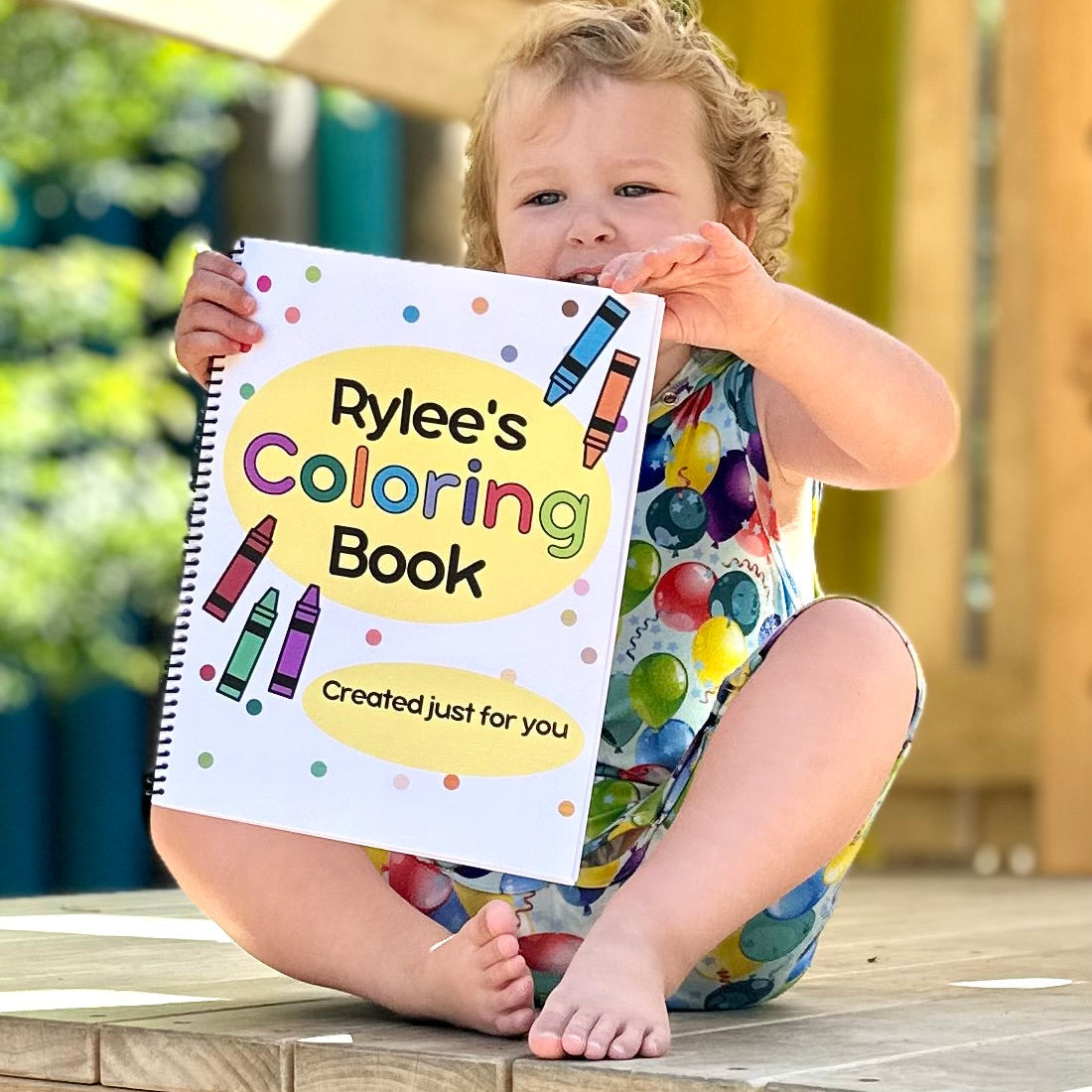 Child holding a coloring book titled 'Rylee's Coloring Book' outdoors